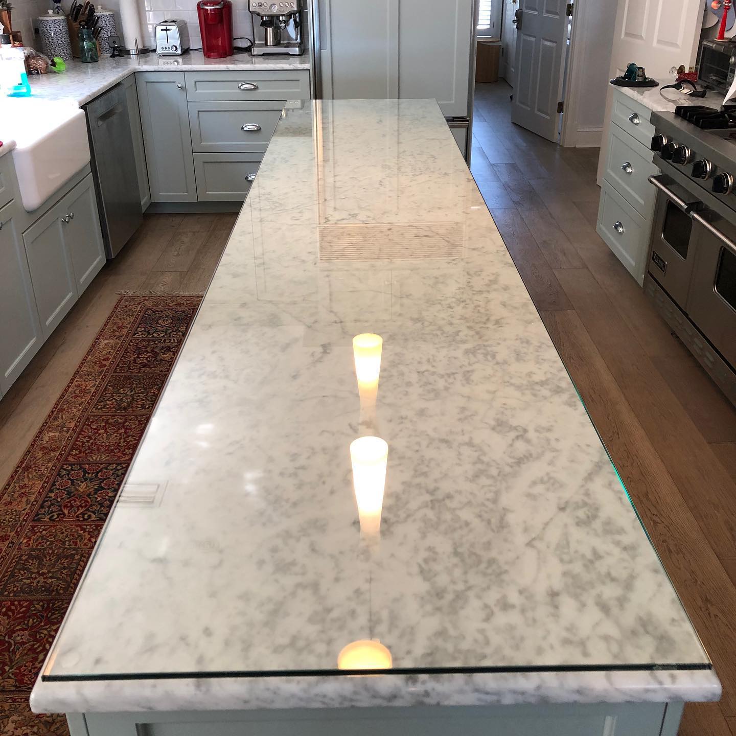 Kitchen island with a polished marble countertop under a glass protective surface reflecting pendant lights.